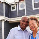 older couple in front of grey house